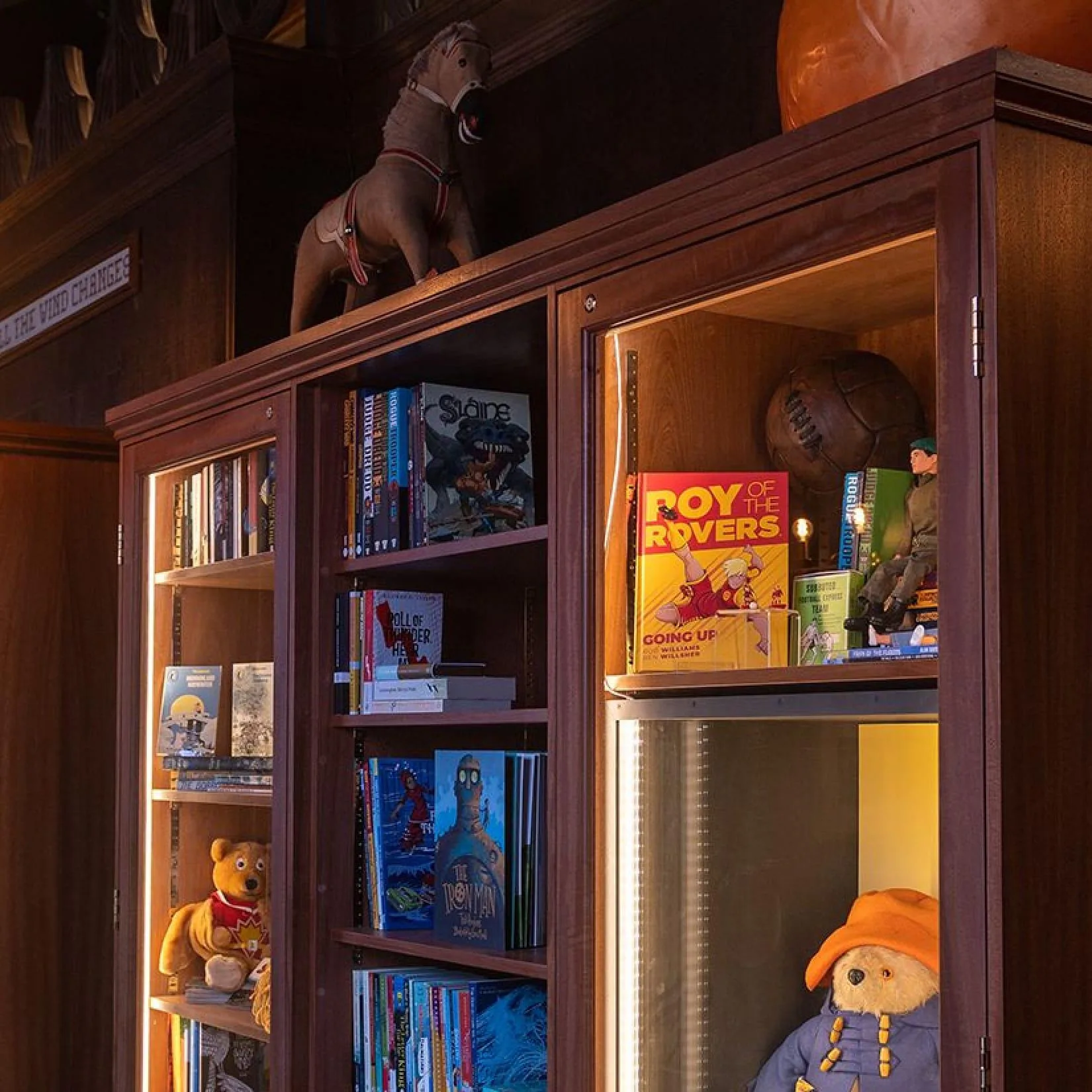 A lit up book shelf featuring books and ornaments.
